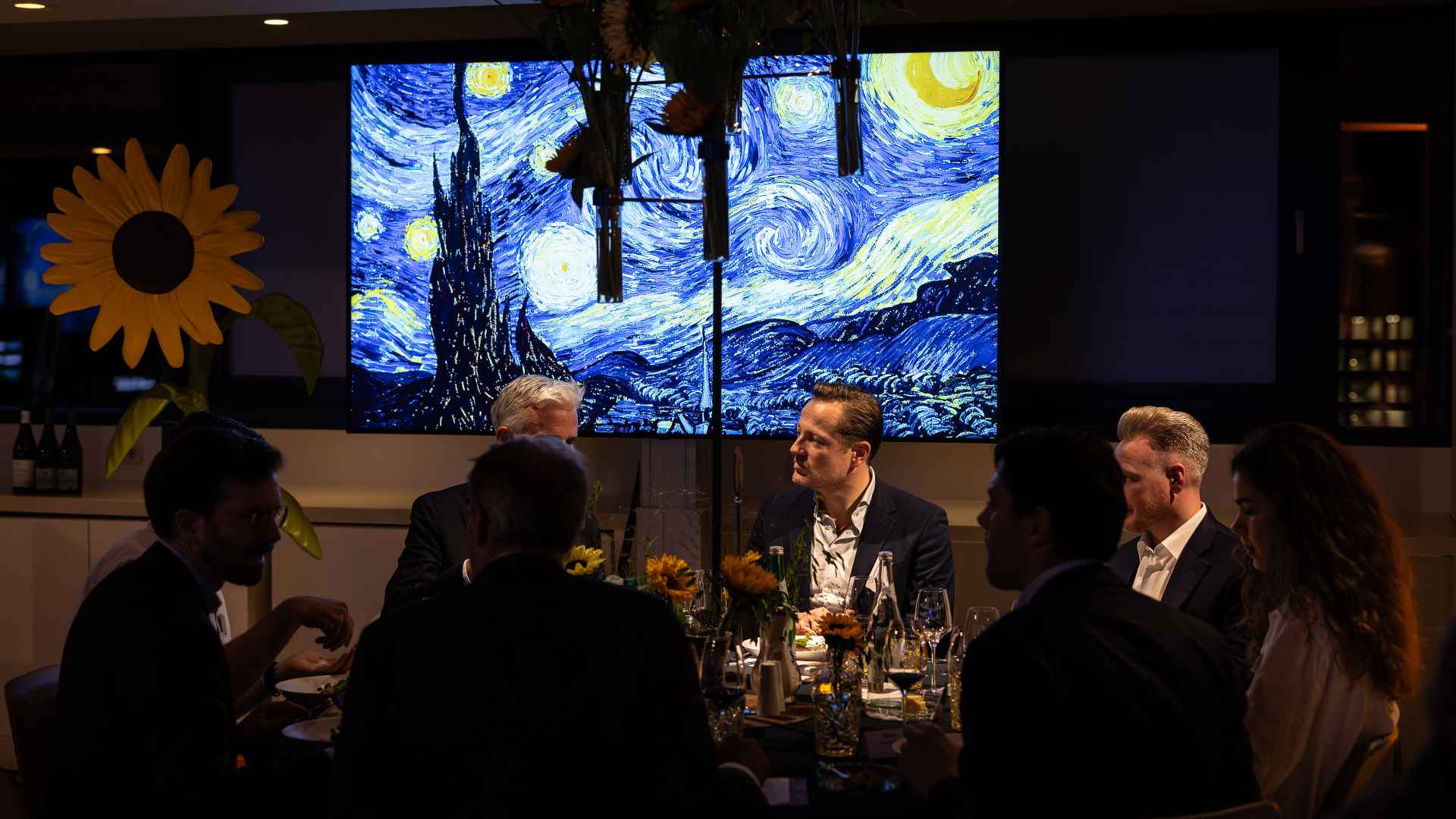 Corporate dinner with ambient lighting and artistic screen backdrop in luxury event setting
