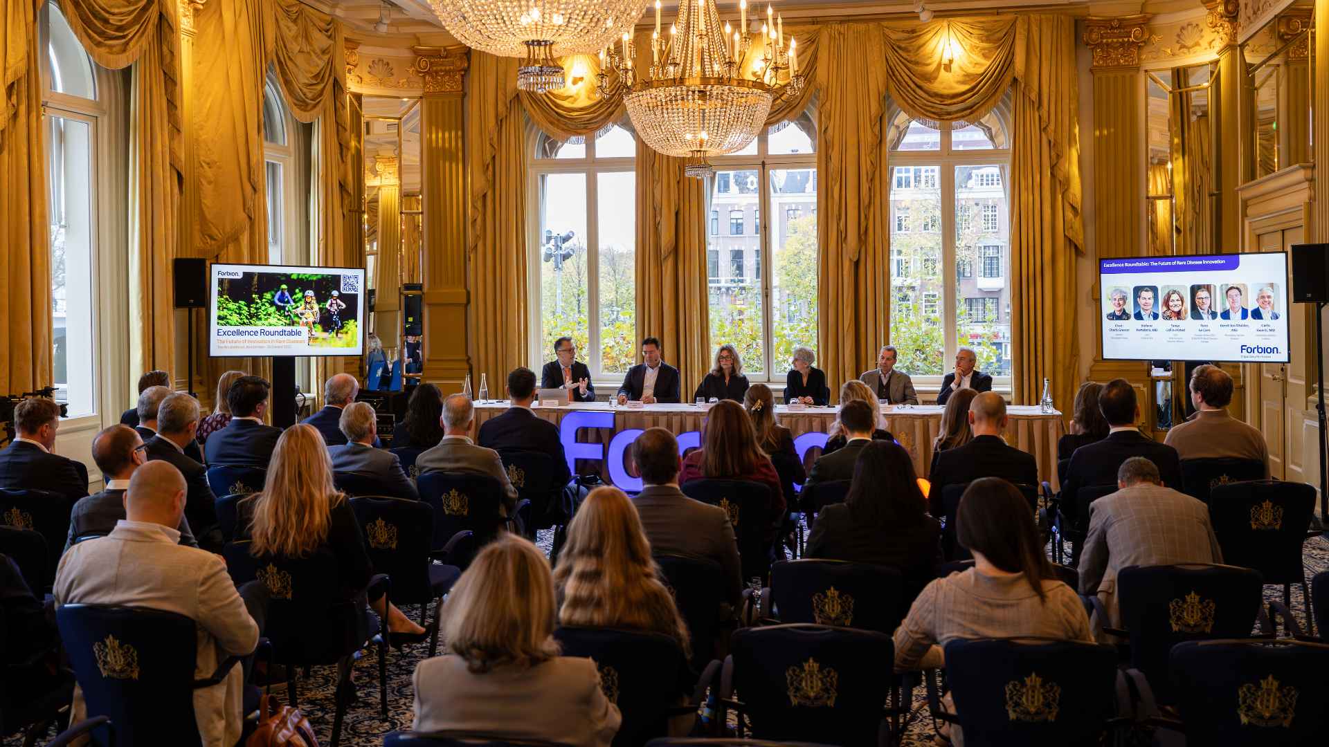 Executive panel discussion at corporate event in luxury ballroom with chandelier and formal seating
