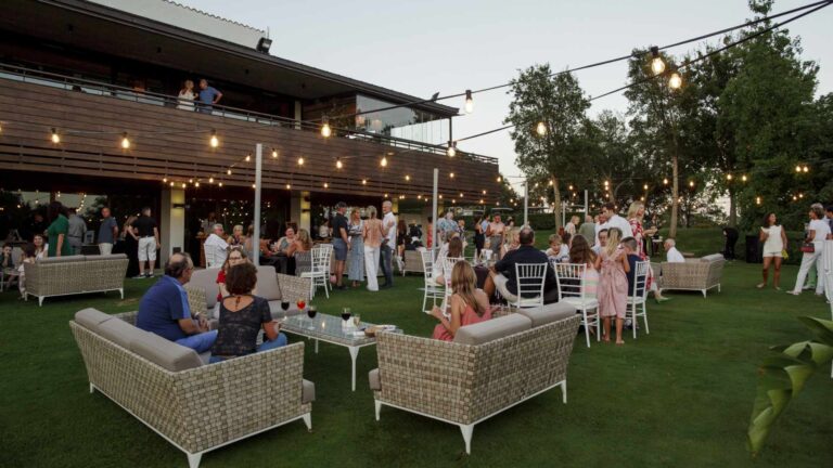 Corporate networking event in an outdoor garden venue with ambient lighting, lounge seating, and social gathering atmosphere
