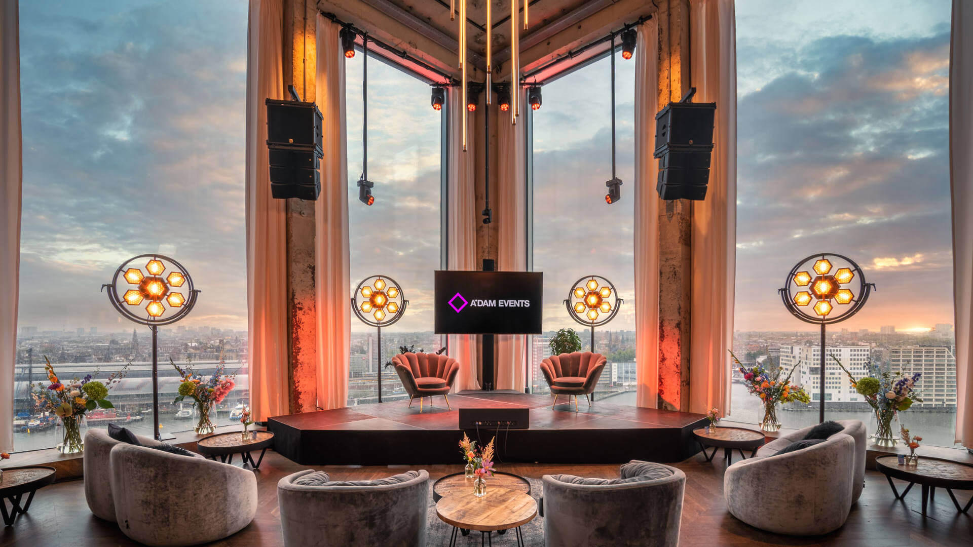 Branded corporate event stage with lounge seating, lighting setup, and panoramic city backdrop