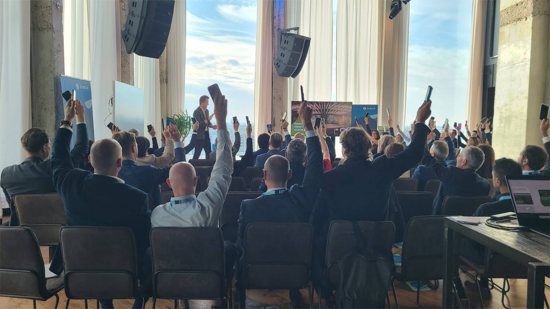 Corporate conference audience actively participating and raising hands during a keynote presentation