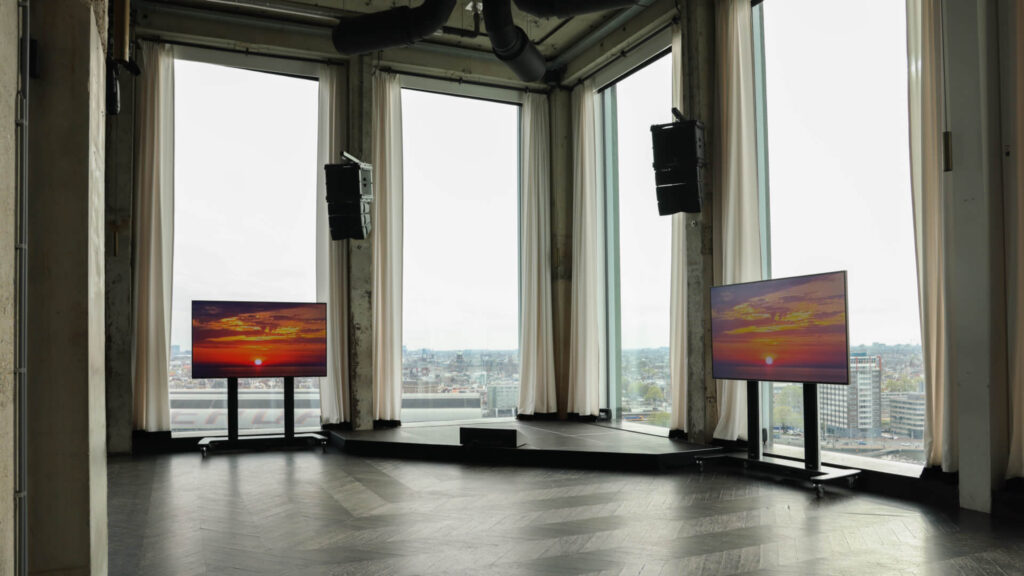 Modern corporate event stage setup with screens and panoramic city view through floor-to-ceiling windows
