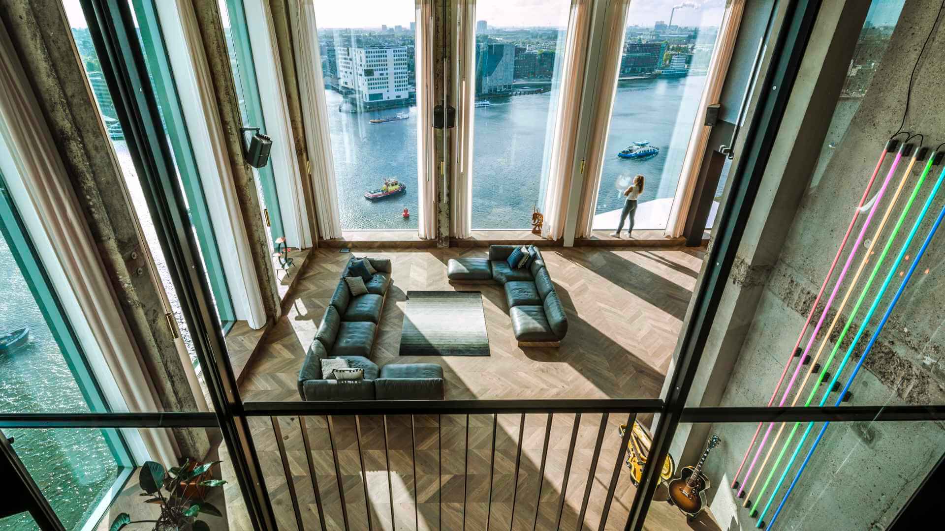 Modern Amsterdam conference venue interior with floor-to-ceiling windows overlooking the IJ harbour, herringbone wood floors, and contemporary furnishings suited to corporate events and meetings.
