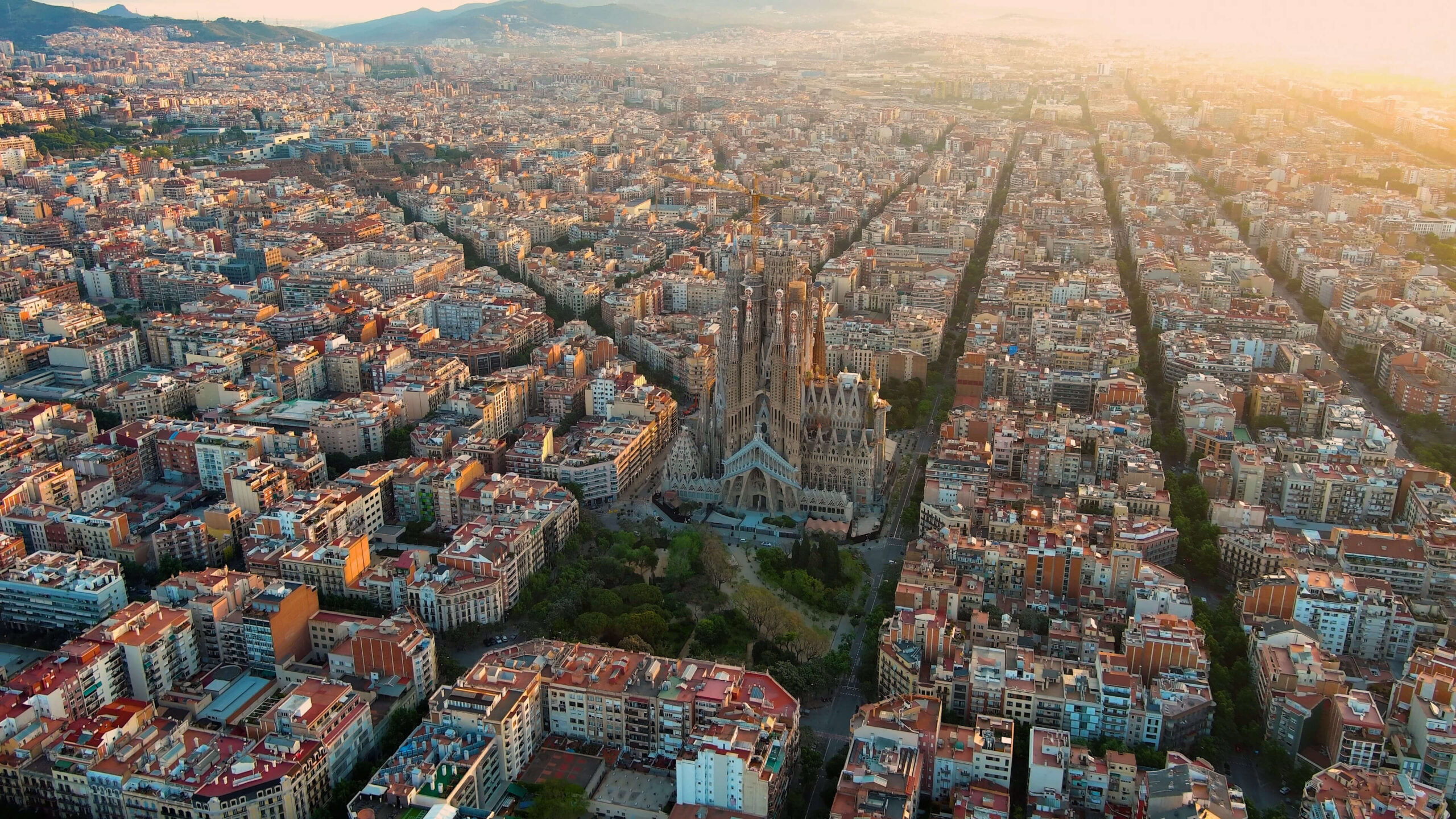 Aerial view of Barcelona's Eixample district at golden hour with the Sagrada Família at its centre and the city's octagonal grid extending towards the mountains — a premier European corporate event destination.