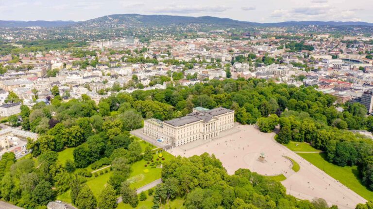 Aerial view of Oslo's Royal Palace and its surrounding Palace Park on a clear summer day, with the neoclassical building set within an expanse of green parkland in the heart of the Norwegian capital.
