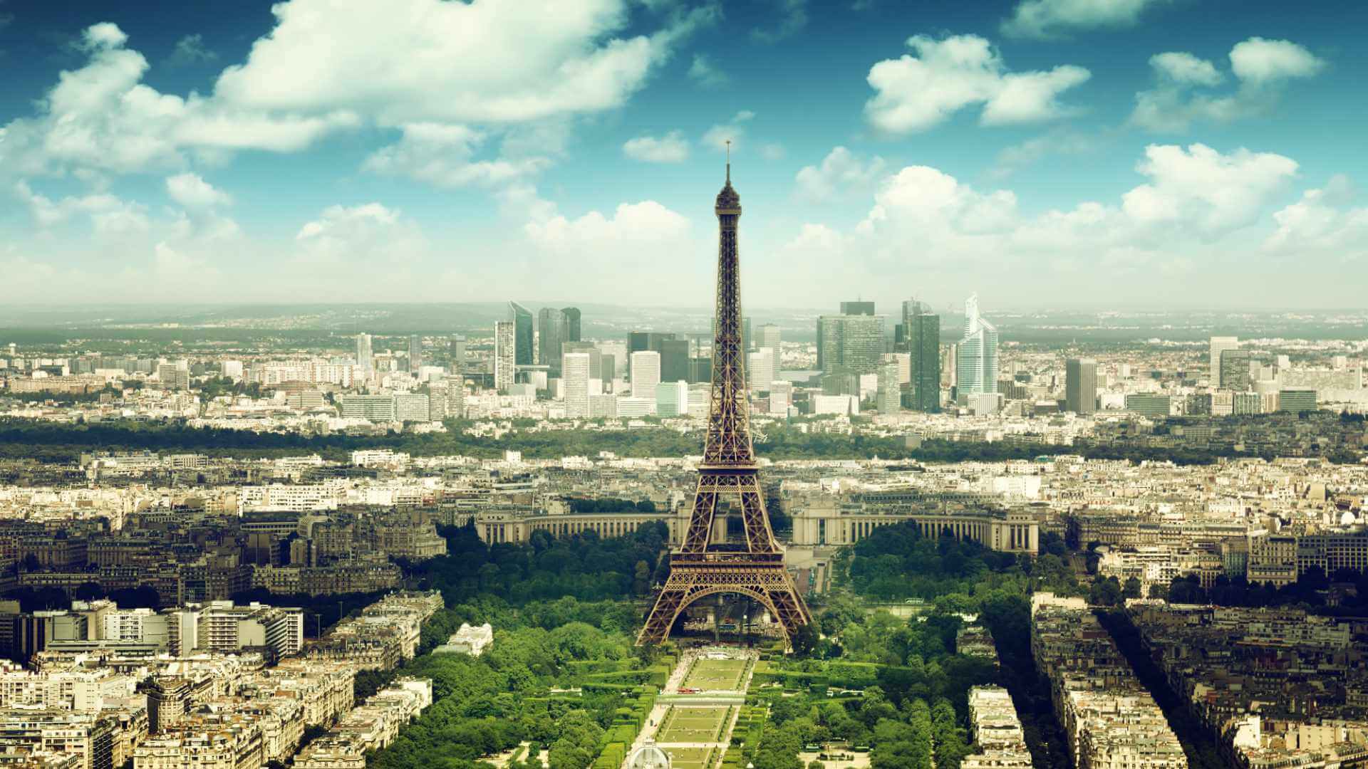Aerial view of Paris with the Eiffel Tower at its centre, the Champ de Mars below, and the La Défense business district on the horizon — one of Europe's most iconic corporate event destinations.