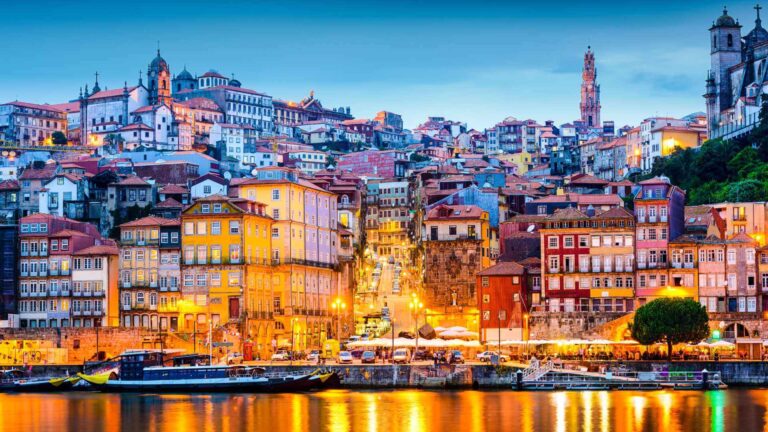 Porto's colourful Ribeira district illuminated at night with warm golden facades reflected in the Douro river, showcasing the Portuguese city as an atmospheric corporate event destination.