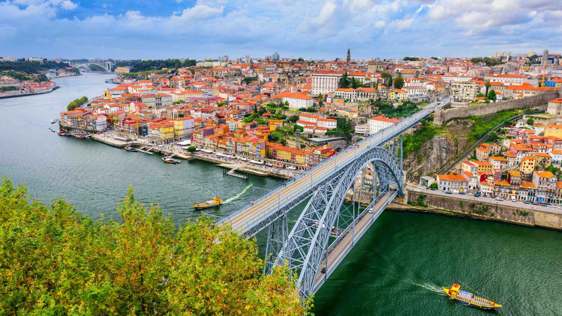 Aerial view of Porto with the iconic Dom Luís I iron bridge spanning the Douro river and the city's colourful old town rising up the hillside above the riverbank.