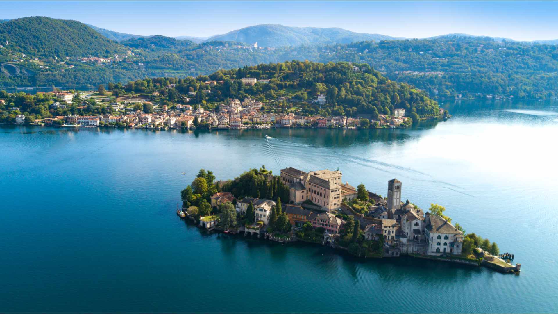 Aerial view of Isola San Giulio on Lake Orta in northern Italy, with its medieval monastery surrounded by serene alpine water and the hillside village of Orta San Giulio on the shore behind.