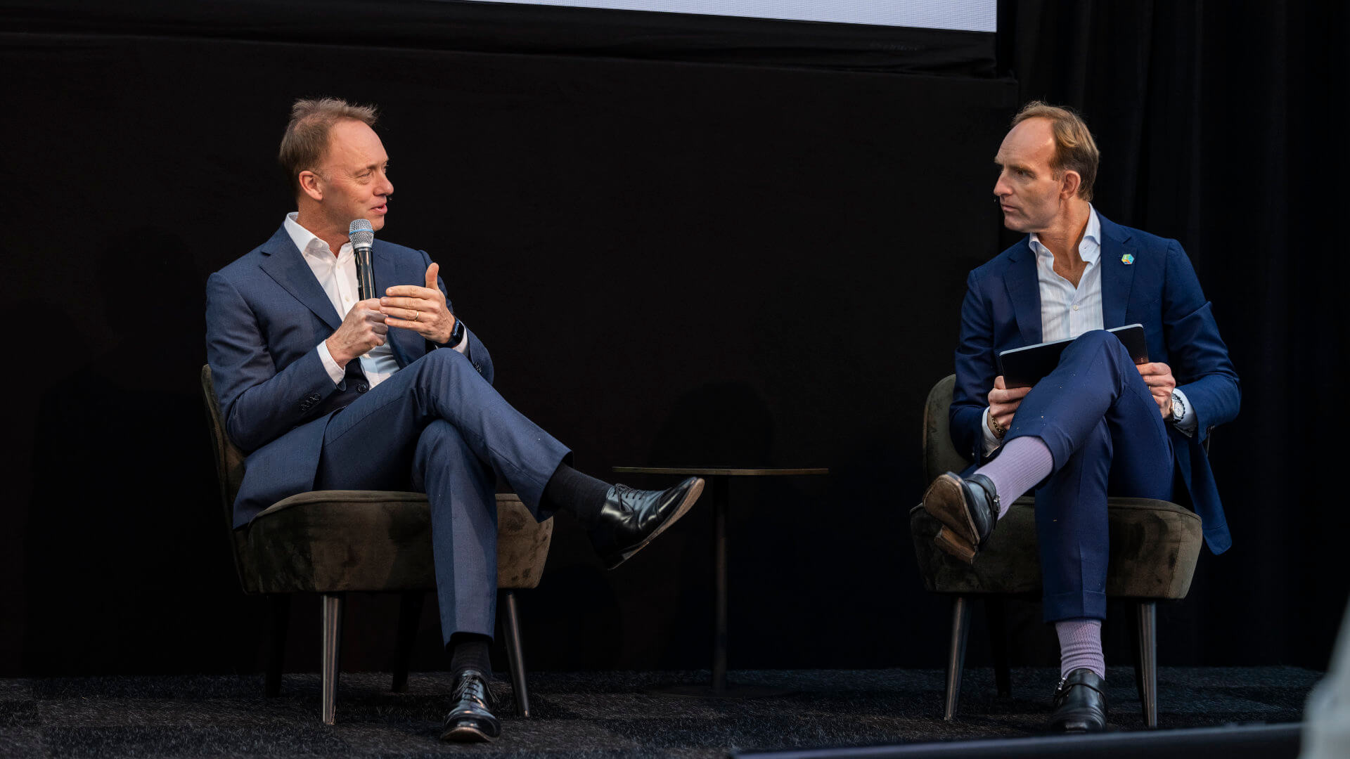 Two professionals in a candid on-stage conversation at a corporate event, one speaking directly into a microphone while the other listens — the quality of direct, unhurried exchange that separates a reliable incentive travel agency from a confident but ultimately thin pitch.
