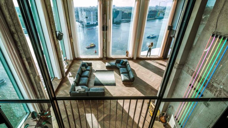 Interior of a contemporary double-height event space in Amsterdam with floor-to-ceiling windows overlooking the IJ waterway and the Eye Film Museum across the water — strategic venue selection that places the destination directly inside the guest experience.