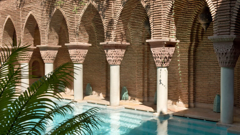 La Sultana Marrakech — ornate Moorish arched pool with intricate brick columns and turquoise water, illustrating the type of hotel property whose location must be matched to the programme's geography before rooms are contracted