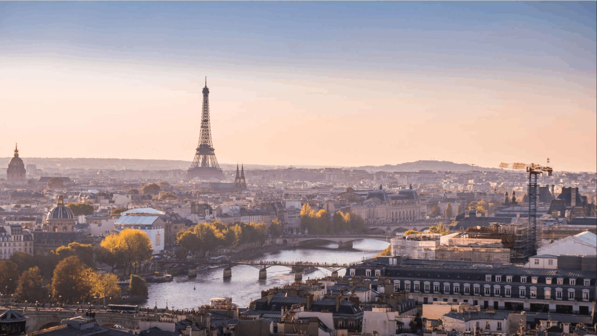 The Paris skyline at golden hour, with the Eiffel Tower rising above the Seine, autumn trees lining the riverbanks and the dome of Les Invalides to the left — the city that offers deep hotel inventory, global flight access and a remarkable concentration of art, gastronomy and heritage for a senior leadership programme.