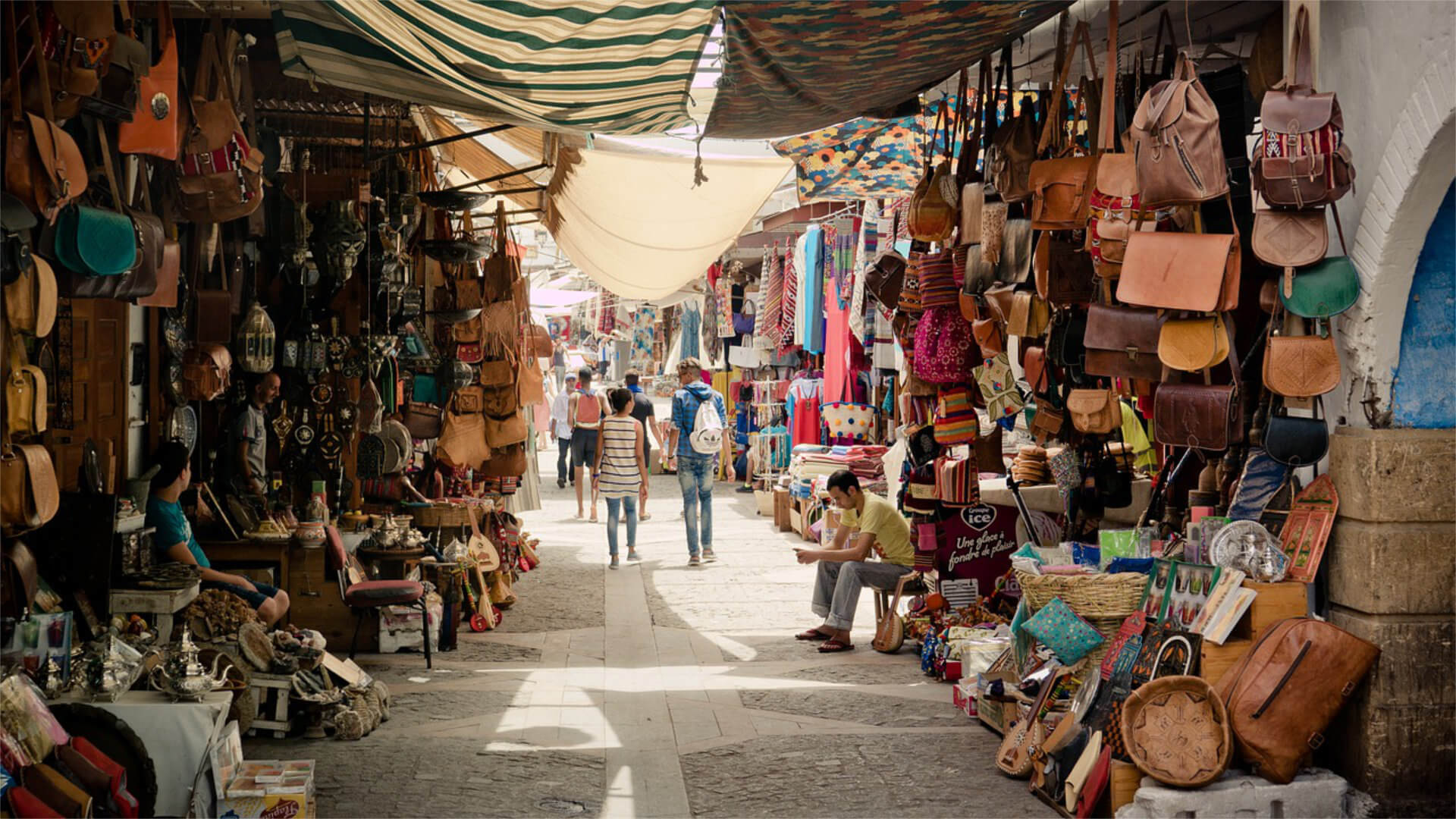 Narrow covered souk lane in the Marrakech Medina lined with leather goods, bags and crafts on both sides — the environment where group movement requires a planned last-mile handover from coaches to guided walking routes with named group hosts