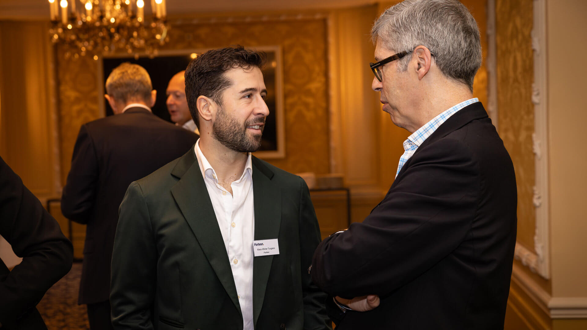 Two senior professionals in close conversation during a networking reception at a grand hotel — the quality of unstructured exchange that a well-sequenced leadership programme creates when purpose, non-negotiables and format are agreed before a single venue is sourced.