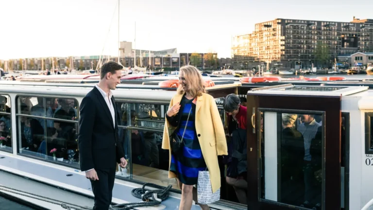 An event host welcoming a guest dockside before boarding a private canal boat for a corporate programme in Amsterdam — the kind of personal arrival moment that only happens when one party has clear, unambiguous ownership of the complete guest journey.