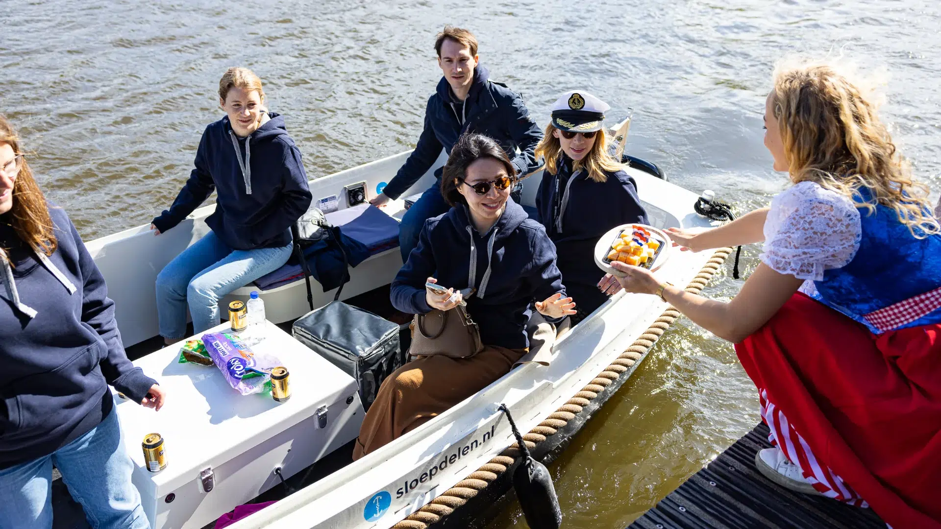 Corporate group on a self-drive Amsterdam canal boat with a host in Dutch costume offering local snacks — an activity that works because it uses the city's waterways naturally rather than adding an exercise disconnected from the destination