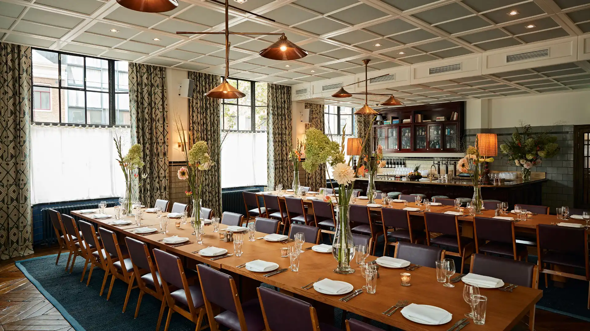 Private dining room set for a group arrival dinner with long communal tables, copper pendant lamps and fresh flower centrepieces, showing how a well-chosen restaurant makes day one feel like the programme has already started