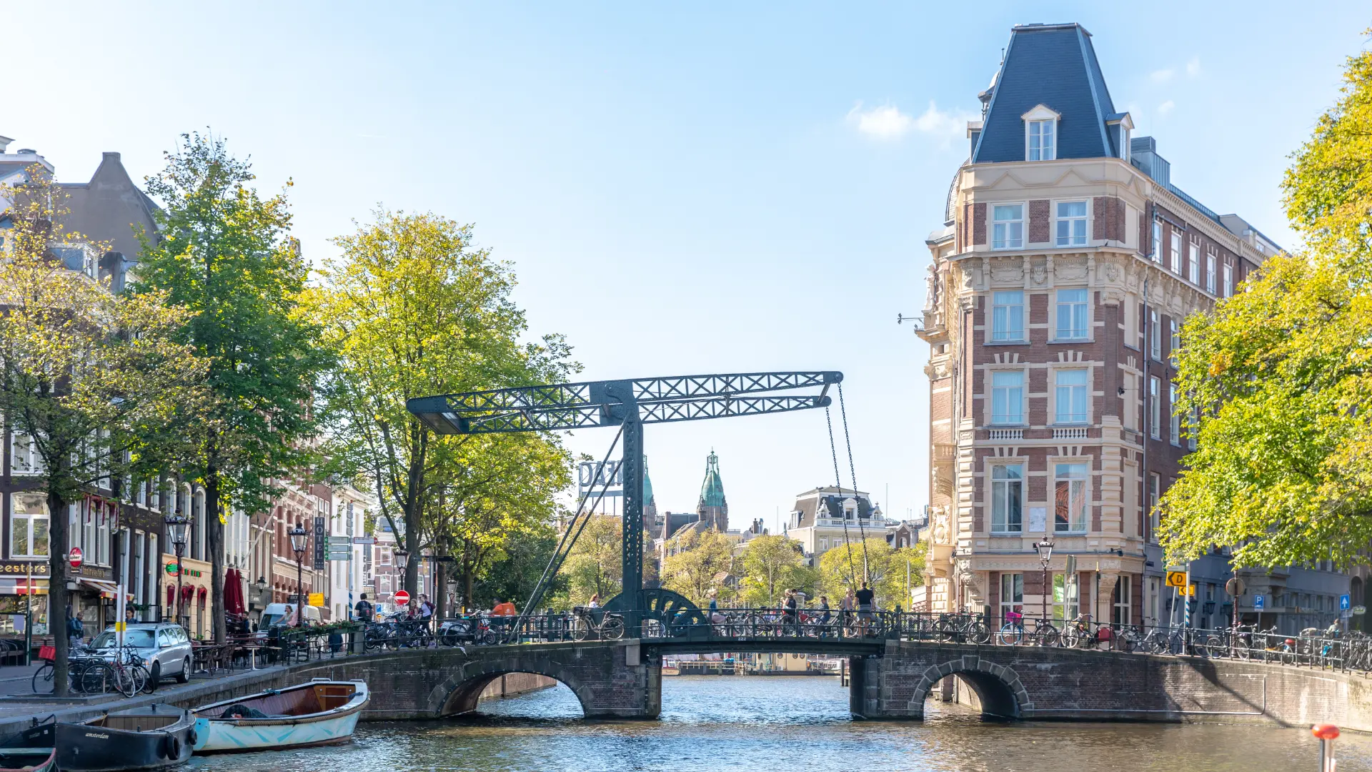 Amsterdam drawbridge over a canal in autumn with a historic corner building and cyclists crossing — the kind of city infrastructure that looks straightforward on a map but can affect every group transfer if routes are not tested before venues are signed